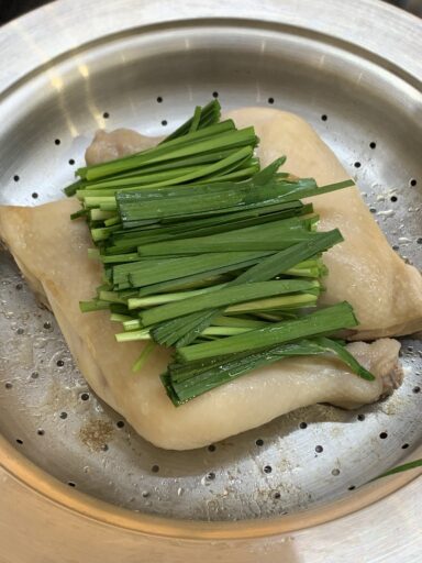 North Korean-style braised chicken being steamed with chives on top in a steamer