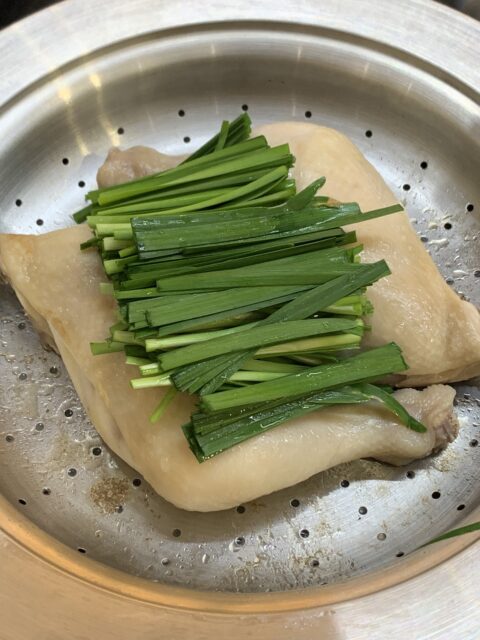 North Korean-style braised chicken being steamed with chives on top in a steamer