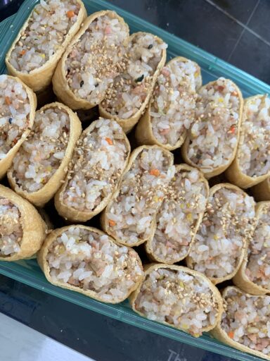 Korean yubu chobap recipe with rice-filled tofu pockets in a lunchbox, topped with sesame seeds