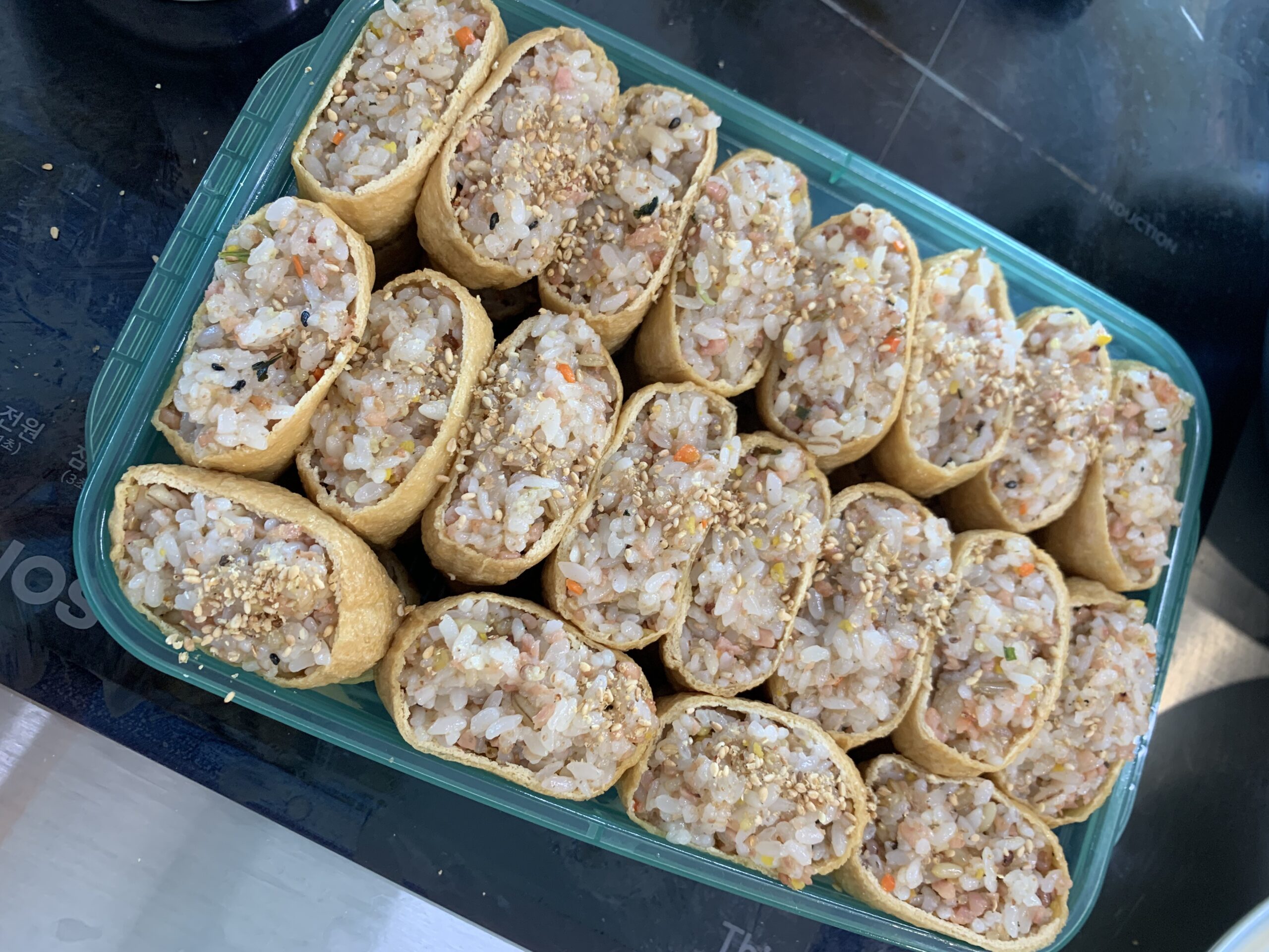 Korean yubu chobap recipe with rice-filled tofu pockets in a lunchbox, topped with sesame seeds